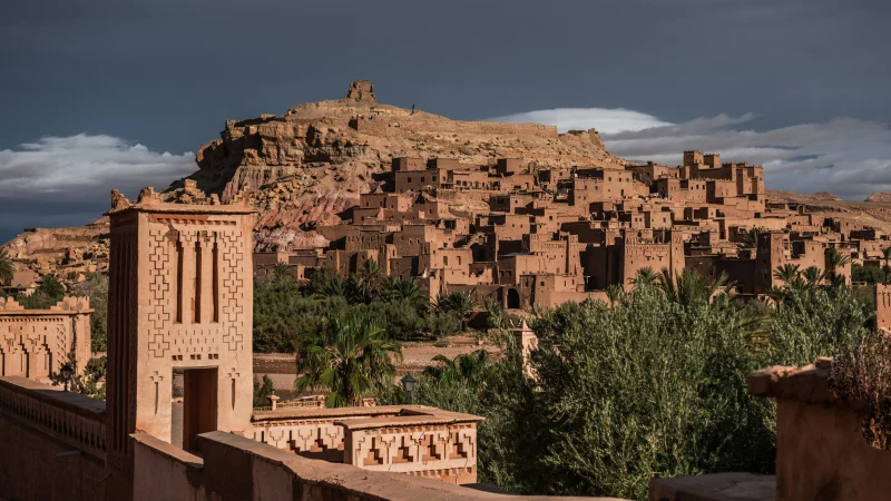 Traditional mud-brick village of Aït Benhaddou with its fortified walls and towers set against desert hills and dramatic skies in southern Morocco.